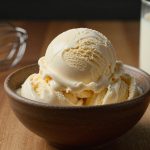 A scoop of vanilla ice cream in a bowl beside a whisk and open can.